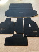 Full set of five black carpet mats for Lexus RX350 (2010) on beige carpet background, showing all floor and trunk mats