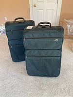Front view of two large Samsonite suitcases standing upright on carpet, showing front multiple zippered compartments and top handles.