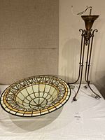 Complete Tiffany style pendant light with stained glass bowl on the table and metal frame standing upright next to it.