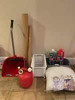 Photo showing all items in the lot arranged against a wall: red heavy duty dustpan, red gas tank, white metal Elfa pullout drawer, rolls of contractor paper, gray tool caddy with organizer drawer, and two bottles of Zep Drain Care in the caddy, plus the curved cushion insert in packaging on the floor.
