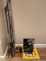 Photo showing six street hockey sticks, one goalie stick, wooden carrier with hockey pucks and tape, Rollerblade Quantum inline skates size 9, Bruins rally towels