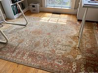 Full view of the gold, coral, and beige rug laid out on hardwood floor, showing overall pattern and size under furniture.