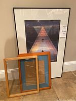 Set of one black framed Paul Klee poster and two wood photo frames on floor.