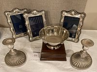 Full set photo showing 3 silver-tone photo frames, 2 silver plated weighted candlesticks, and round silver or silver plated bowl on wooden base.