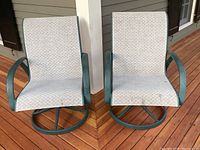 Front view of two swivel outdoor chairs with green metal frames and white patterned fabric seats and backs.