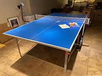 Full view of assembled blue table tennis table in basement