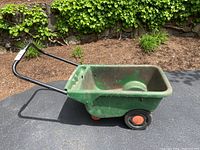 Side view of green Scotts plastic tub yard cart wheelbarrow with black handles and two wheels.