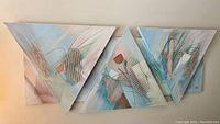 Set of three triangular abstract pastel textured canvas artworks hanging on the wall.