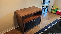 Credenza with closed top showing wood grain, lower open shelf, and black cupboard doors.