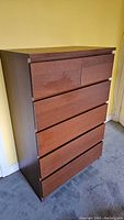 Angled side view of IKEA 6-drawer tall dresser showing dark wood finish and six drawers.