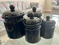 Four black ceramic canisters of different sizes with lids featuring round knobs, displayed on a table in a living room setting.