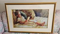 Full view of the framed artwork showing a child reading on a couch, with gold frame and white matting
