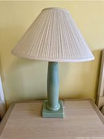Front view of green ceramic table lamp with white fabric pleated shade on wooden surface.