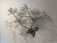 Metal wire wall sculpture resembling branches with a cluster of rounded metal pieces mounted on a wall, showing the overall shape and shadow details.