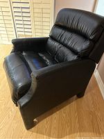 Side angled view showing the left side, seat, cushion and armrest of the black synthetic leather chair with visible wear on seating area and minor creasing.