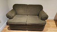 Front view of green love seat showing two seat cushions, rolled armrests, and corduroy upholstery texture.
