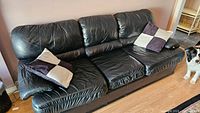Black leather pull out couch with three seat cushions and two throw pillows on a hardwood floor.