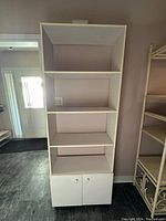 Front view of white shelving unit with four shelves and two cupboards at bottom against wall