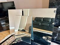Three rectangular mirrors, two large and one smaller, arranged on a carpeted floor in a living room area.