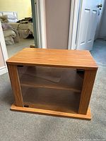 Wooden TV stand front view showing glass door and interior shelf on carpeted floor.