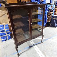 Full view of antique curio cabinet showing glass front doors and curved legs.
