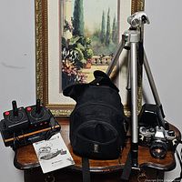 Overview photo showing Atari Flashback 7 console with two joysticks, user manual, Olympus OM-10 camera on tripod, and camera carrying bag.