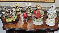 Overview of nine bird-themed figurines and music boxes of various colors and designs displayed on a wooden table.