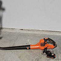 Full side view of the Black & Decker cordless leaf blower with battery and charger laid on concrete floor.
