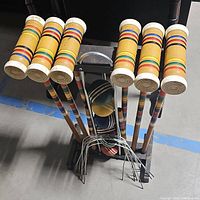 Overall front view of six wooden mallets in stand, showing colorful stripes, mallet heads, and croquet balls stored below.