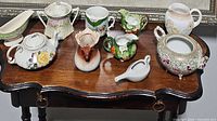 Table display with assorted decorative porcelain items including pitchers, teapot, gravy boat, and cachepot.