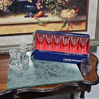 Set of 6 crystal glasses in original box with a green marble serving board and several textured clear glass candle holders on wooden table.