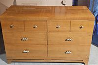 Front view of the wood dresser showing six drawers with diamond-patterned and simple metallic handles, slight wear visible on the surface.