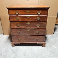 Front view of the wooden dresser showing five drawers with brass handles and wear on the finish.