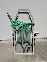View of plastic hose reel holding grey hose with green hose coiled on handle and blue nozzle attached.