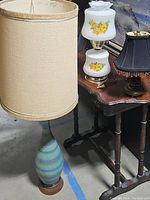 Three assorted lamps on a wooden table and floor showing different styles and materials