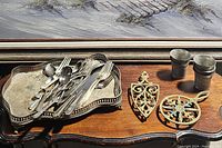 Metal tray holding assorted metal flatware and two decorative metal trivets on a wooden surface.