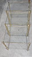 Three gold framed glass nesting tables stacked inside one another, laid flat on floor.