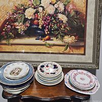 Photo showing three stacks of assorted plates in floral and classic artistic designs of various sizes on a wooden table.