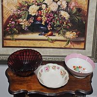Three serving bowls displayed on a wooden surface with a floral painting background, showing variety in design and color.