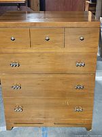 Front view of tall wooden dresser showing three smaller top drawers with metal knobs and three larger drawers below with metal handles. Visible marks and scratches on surface.