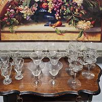 Top view of three sets of vintage glasses arranged on a wooden table with a floral painting background.