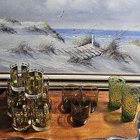 Photo showing three sets of glasses on wooden surface with beach painting in background