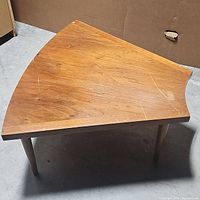 Front angle view showing wooden triangular table with scratches and wear on the surface.