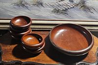 Photo showing one large wood serving bowl and six small wood dishes stacked together beside it on a wooden surface.