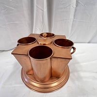 Front top angle view showing polished copper cylindrical wells and central covered opening with knob handle