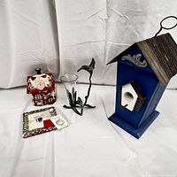 Side view showing blue wooden birdhouse, ceramic house figurine, metal hummingbird candle holder, and ceramic magnet pack