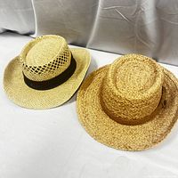 Two straw hats placed side by side showing the full shape and woven texture of each hat.