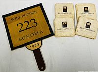 Wooden wine auction paddle serving board with four marble coasters showing Alpha Omega logos