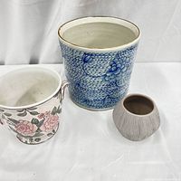 Three pottery planters together: largest blue and white floral, floral handled white planter, and small grey textured planter