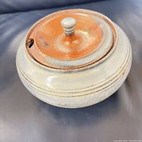 Closed view of the round stoneware bowl with a reddish-brown glazed lid showing the knob handle and notch.